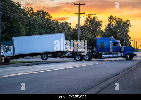 Mobile blaue Pannenhilfe leistungsstarker Abschleppwagen Sattelzugmaschine Abschleppen gebrochen nach Unfall Tag Kabine Sattelzugwagen mit Kastenanhänger fährt auf der Straße Stockfoto