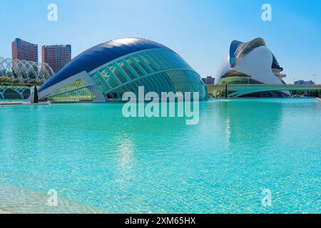 Glitzerndes Wasser umgeben bemerkenswerte Gebäude der Stadt der Künste und Wissenschaften mit zeitgenössischem Design vor dem Hintergrund der Skyline von Valencia Stockfoto