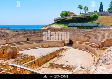 Die antiken Amphitheater-Ruinen in Tarragona zeigen architektonische Pracht, umgeben von grünen Hügeln und dem glitzernden Meer an einem sonnigen Sommertag. Stockfoto