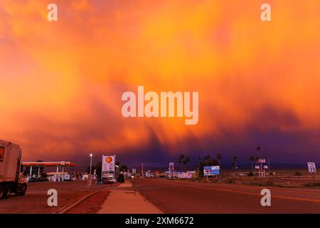 Baker, Kalifornien - 15. April 2024: Leuchtende Orange- und Violetöne erleuchten den kalifornischen Himmel während des Sonnenuntergangs. Westamerikanische Straßenlandschaft. Stockfoto