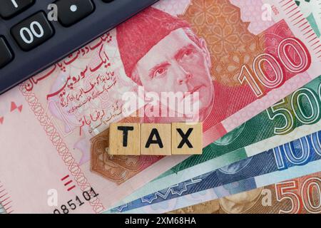 Holzblöcke STEUERWORT auf pakistanischen Banknoten mit Taschenrechner. Steuerkonzept. Stockfoto