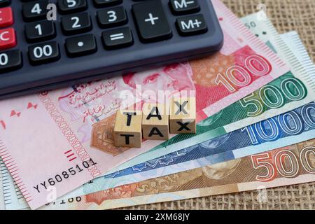 Holzwürfel mit dem Wort Steuer auf pakistanische Rupien mit Rechner. Steuern in Rupien. Stockfoto