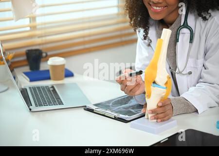 Lächelnde Ärztin, die die Struktur des Kniegelenks am Anatomiemodell bei Online-Sprechstunde demonstriert Stockfoto