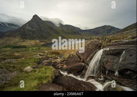 Kleiner Wasserfall mit Tryfan und See Ogwen im Hintergrund an einem bewölkten Tag, Snowdonia National Park, Nordwales, Großbritannien. Stockfoto