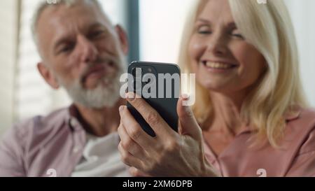 Glückliche Familie lächelndes älteres reifes kaukasisches Paar älterer Ehemann Mann männliche Frau Frau Frau weibliche Benutzung Handy Smartphone Ferneinkaufen Internet Stockfoto