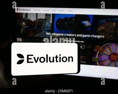 Person, die ein Smartphone mit dem Logo des schwedischen Glücksspieltechnikunternehmens Evolution ab vor der Website hält. Schwerpunkt auf dem Display des Telefons. Stockfoto