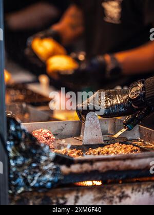 Ein Verkäufer bereitet Burger auf einem Grilltisch an einem Street Food Stand zu Stockfoto