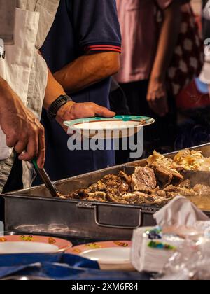 Ein Anbieter serviert Fleisch aus einem großen Metalltablett an einen Kunden Stockfoto