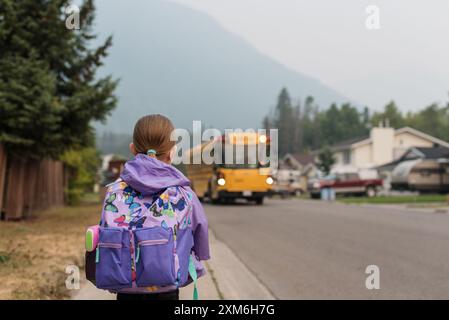 Ein kleines Mädchen mit Rucksack wartet am ersten Schultag auf den Bus. Stockfoto