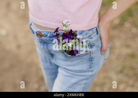 Nahaufnahme eines jungen Tween-Mädchens in Jeans mit Tasche voller Wildblumen. Stockfoto