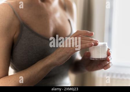 Seniorin in den 60er Jahren, die Handcreme auf die Haut der Hände pflegt Stockfoto