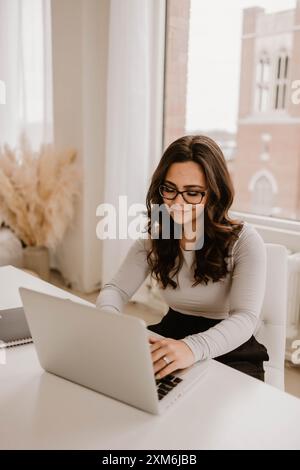 Die junge hispanische Frau arbeitet an einem Schreibtisch mit einem Laptop Stockfoto