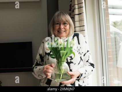 oma hält Blumen in einer Vase an ihrem Geburtstag Stockfoto