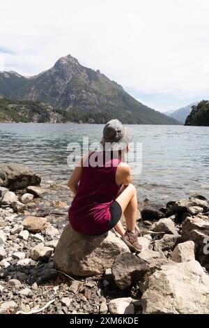 Eine Frau sitzt auf einem Felsen am See und trägt einen Hut Stockfoto