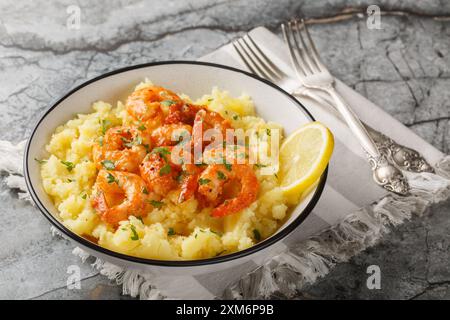Portion Knoblauchgarnelen mit Kartoffelpüree, Zitrone und Kräutern in einer Schüssel auf dem Tisch. Horizontal Stockfoto