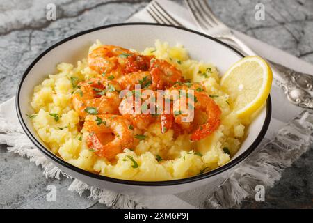 Gebratene Knoblauchgarnelen, serviert mit heißen Kartoffelpüree, Zitrone und Kräutern in einer Schüssel auf dem Tisch. Horizontal Stockfoto