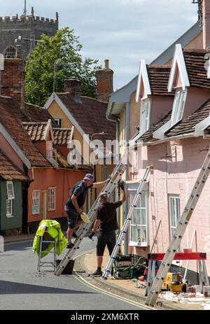 Zwei Arbeiter steigen Leitern auf einer angenehmen Renovierung eines Cottages in der Castle Street Framlingham mit dem Kirchturm von St. Michael's im Hintergrund. Stockfoto