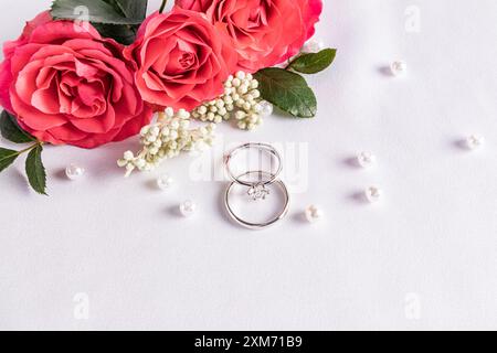 Zartes Hochzeitsarrangement mit zwei Hochzeit Platin Ringen auf weißem Satin Hintergrund mit Perlen und Blumen. Postkarte. Einladung. Abdeckung. Stockfoto