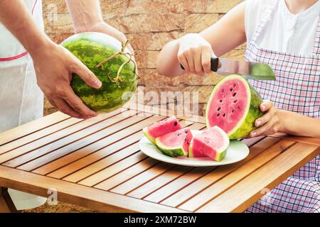 Junge Frau in Schürze, die frische, saftige rote Wassermelone schneidet Stockfoto