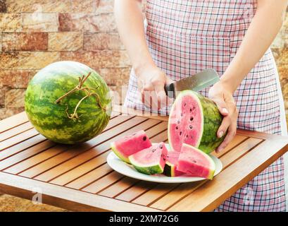 Junge Frau in Schürze, die Wassermelone auf Holztisch schneidet Stockfoto