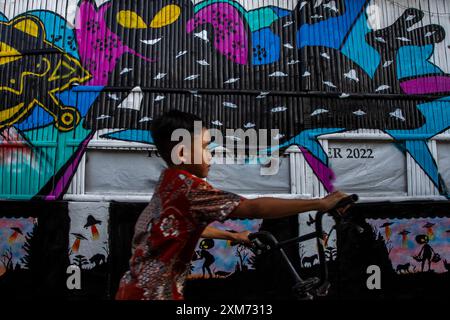 26. Juli 2024, Yogyakarta, Spezialregion Yogyakarta, Indonesien: Ein Kind fährt mit dem Fahrrad in der Nähe eines Wandgemäldes mit UFO und Alien-Motiven im UFO-Dorf im Mantrijeron District, Yogyakarta City. Die Bewohner arbeiteten zusammen, um das Dorf mit einem UFO- und Alien-Thema zu dekorieren, um den Unabhängigkeitstag der Republik Indonesien am 17. August zu begrüßen. Darüber hinaus ist das UFO-Dorf als Sprache für das Studium des Universums gedacht, so dass die Menschen sich immer bewusst sind, in ihrer jeweiligen Umgebung Sauberkeit zu wahren. (Foto: © Angga Budhiyanto/ZUMA Press Wire/Alamy Live News) EDITO Stockfoto