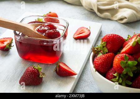 Glas Erdbeermarmelade in Holzlöffel auf weißem rustikalem Tisch Stockfoto