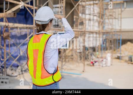 Junge Bauarbeiterin mit Schutzhelm und Sicherheitsweste, die Baumaterialien auf einer Baustelle inspiziert. Stockfoto