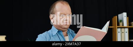 Ein Mann mit Inklusivität sitzt nachdenklich, vertieft in ein Buch, sein Blick fixiert auf die offenen Seiten. Stockfoto