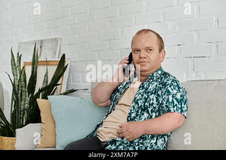 Ein Mann mit Inklusivität, der ein Hemd mit Blumenmuster trägt, sitzt auf einer Couch und spricht telefonisch. Stockfoto