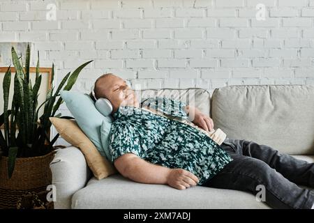 Ein Mann mit Inklusivität entspannt sich auf einer grauen Couch mit weißem Backsteinmauerhintergrund. Stockfoto