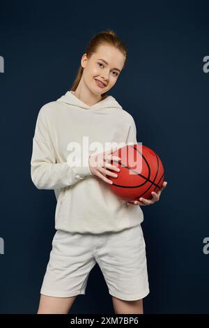 Frau in weiß lächelt mit rotem Basketball auf blauem Hintergrund. Stockfoto
