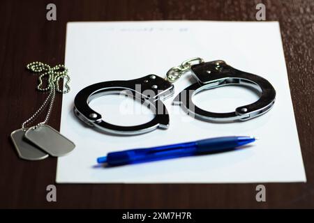 Handschellen und ein Armeeabzeichen auf weißem Papier, mit einem blauen Stift in der Nähe Stockfoto