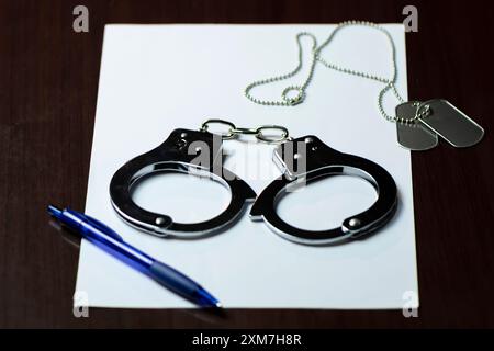 Handschellen und ein Armeeabzeichen auf weißem Papier, mit einem blauen Stift in der Nähe Stockfoto
