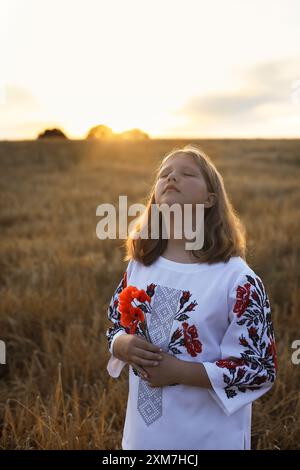 Baby mit ukrainischen Accessoires im Mohnfeld bei Sonnenuntergang Stockfoto