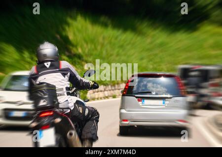 Italien - 21. Juli 2024: Ein Motorradfahrer fährt auf einer kurvenreichen Straße gefährlich nahe an einem Auto, was auf eine mögliche Unfallgefahr hinweist. Symbolische Imagerisiken und Gefahren im Straßenverkehr, insbesondere für Motorradfahrer *** ein Motorradfahrer fährt gefährlich nahe an einem Auto auf der Gegenfahrbahn auf einer kurvigen Straße, was auf eine potenzielle Unfallgefahr hinweist. Symbolbild Risiken und Gefahren im Straßenverkehr, insbesondere für Motorradfahrer Stockfoto