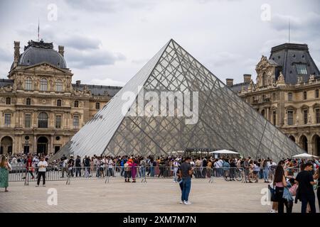 Paris, Frankreich - 14. Juli 2024: Vor dem Louvre in Paris stehen zahlreiche Touristen aus aller Welt vor der berühmten Glaspyramide, ein berühmtes Wahrzeichen der Stadt *** vor dem Louvre-Museum in Paris stehen zahlreiche Touristen aus aller Welt in einer Warteschlange vor der ikonischen Glaspyramide, einem berühmten Wahrzeichen der Stadt Stockfoto