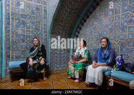 Drei Frauen in traditioneller Kleidung sitzen in einem reich gefliesten Raum mit komplizierter persischer islamischer Architektur Stockfoto