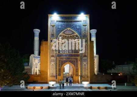 Nächtlicher Blick auf den beleuchteten Eingang des Gur-e-Amir Timur Mausoleums in Samarkand, Usbekistan, mit komplizierten Mosaikmustern und Besuchern, die zu Fuß gehen Stockfoto