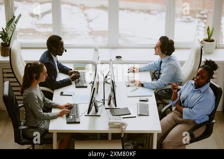 Birassisches Team von Bedienern, die Computer verwenden und Kopfhörer im Callcenter tragen Stockfoto