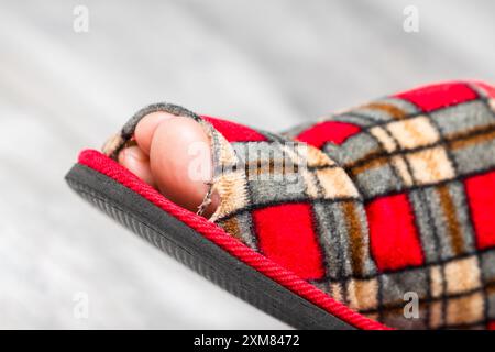 Ein Fuß in einen alten, undichten Slipper. Alter Pantoffel. Sneaker mit Lochmuster. Die Spitze ragt aus dem Schuh im Slipper heraus Stockfoto