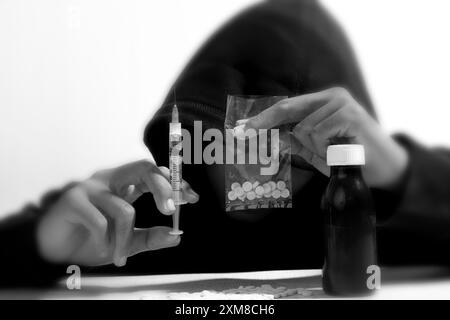 Mann in Hoodie Drogensüchtig, mit Drogen Ecstasy Pillen, Spritze, harte Drogen Überdosis und Suchtkonzept, Schwarz-weiß-Foto Stockfoto