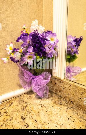 Rosafarbene und lila Kunstblumen in einer Vase, die sich im Spiegel auf der Marmortheke eines Damentoiletts widerspiegelt Stockfoto