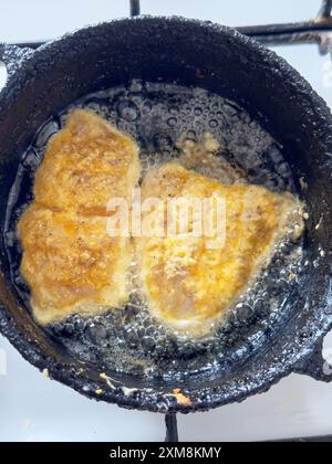 Nahaufnahme von zwei frittierten Fischstücken, die in einer gusseisernen Pfanne kochen Stockfoto