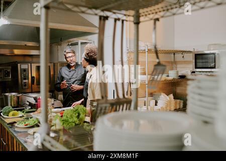 Zwei hochqualifizierte Köche stehen in der Mitte der Restaurantküche und diskutieren den Kochprozess des berühmten Gerichts Stockfoto