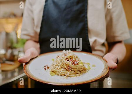Mittlere Nahaufnahme einer runden Keramikplatte mit Spaghetti-Carbonara, bedeckt mit parmigiano, nicht erkennbare männliche Handhalteplatte Stockfoto