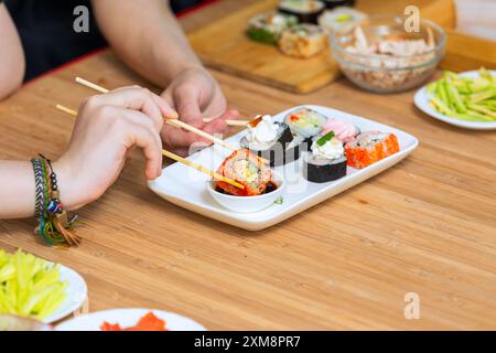 Nahaufnahme von weiblichen Händen, die Stäbchen halten und Sushi-Brötchen essen. Stockfoto