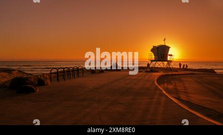 Silhouetten von Menschen um einen Rettungsschirm-Turm, der einen lebhaften Sonnenuntergang über dem Pazifik genießt, Cardiff-by-the-Sea, Kalifornien, USA. Stockfoto
