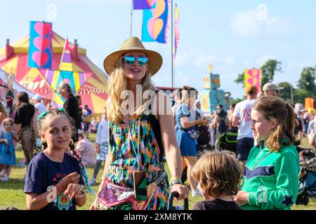 Lulworth, Dorset, Großbritannien. Juli 2024. Mutter mit drei kleinen Kindern, die bunte Latzhose, Sonnenbrille und Strohhut tragen, lächelnd beim Camp Bestival Familienfest, 26. Juli 2024, Credit: Dawn Fletcher-Park/Alamy Live News Stockfoto