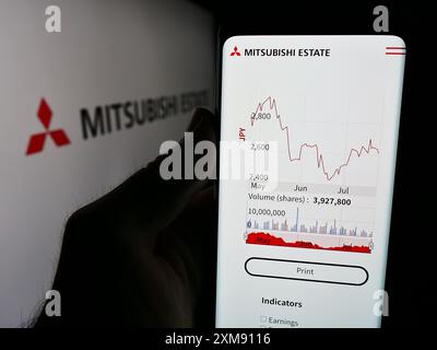 Person mit Smartphone und Webseite der japanischen Immobiliengesellschaft Mitsubishi Estate Co. Ltd. (MEC) mit Logo. Konzentrieren Sie sich auf die Mitte des Telefondisplays. Stockfoto