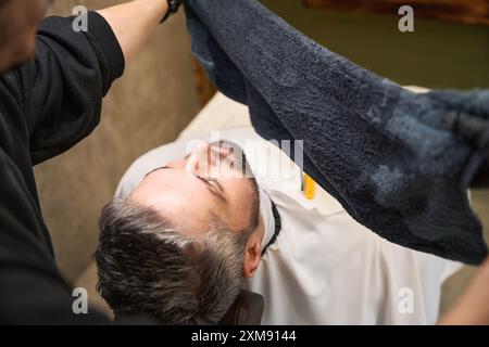 Friseur bereitet heißes Handtuch vor, um es auf Kinn und Hals des Kunden aufzutragen Stockfoto